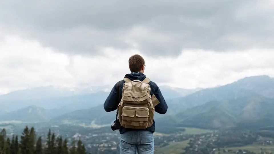 Traveler with a backpack looking out over a vast mountain valley