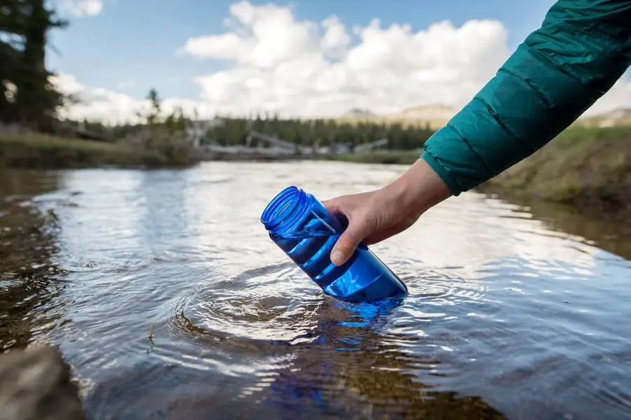 A person refilling a reusable water bottle from a clean stream in the mountains